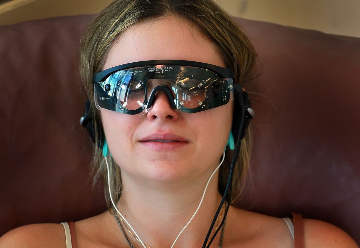 A woman wears light therapy goggles and an Alpha-Stim cranial electrotherapy stimulator.